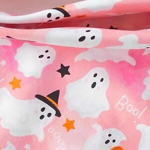 Puede incluir: Tela rosa con tem&aacute;tica de Halloween con fantasmas blancos, estrellas negras y estrellas y calabazas naranjas. Algunos fantasmas llevan sombreros de bruja. La palabra "Boo!" est&aacute; escrita en blanco en la tela.