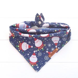 May include: Blue bandana with a white snowflake and Santa Claus pattern. The bandana has a snap closure and a brown leather tag that says "Chumleys".