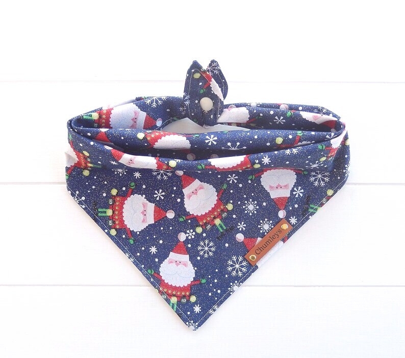 May include: Blue bandana with a white snowflake and Santa Claus pattern. The bandana has a snap closure and a brown leather tag that says "Chumleys".