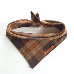 May include: A brown, orange, and green plaid dog bandana with a brown leather tag that says "Chumleys".