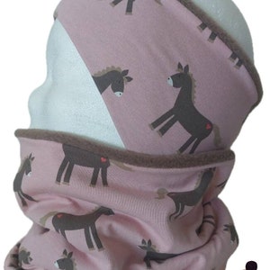 Pode incluir: Cachecol rosa e castanho com forro de lã castanho e um padrão de cavalos com corações. O cachecol está enrolado e um gorro a condizer castanho e branco de bolinhas está no canto inferior direito da imagem.