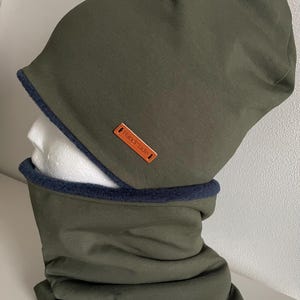 Może przedstawiać: Zestaw zielonego beretu i komina z brązową skórzaną metką z napisem "Handmade".