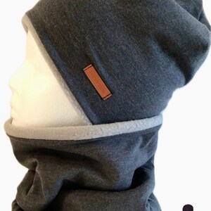 Może przedstawiać: Szary beret z podszewką z polaru i pasującym szarym kominiarką. Beret ma brązową skórzaną metkę z napisem "Handmade". W prawym dolnym rogu zdjęcia widoczny jest mały, beżowy i czarny beret w kropki.