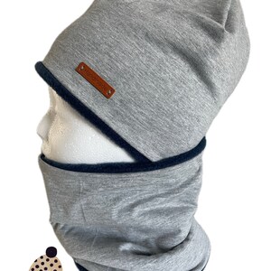 Puede incluir: Gorro gris con forro de lana negro y cuello de lana gris a juego. El gorro tiene una etiqueta de cuero marrón que dice "Handmade".