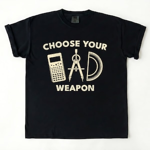May include: Black t-shirt with a distressed graphic that reads "CHOOSE YOUR WEAPON." The graphic features a calculator, a compass, and a protractor. The shirt is made of a soft material and has rolled-up sleeves.