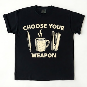 May include: Black t-shirt with the text "CHOOSE YOUR WEAPON" above illustrations of a pen, a steaming coffee mug, and a stapler. The graphic is in a vintage style.
