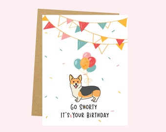 May include: A birthday greeting card featuring a cartoon corgi dog with balloons and colorful bunting. The card reads "Go Shorty It's Your Birthday" in black text. The card has a kraft paper envelope.