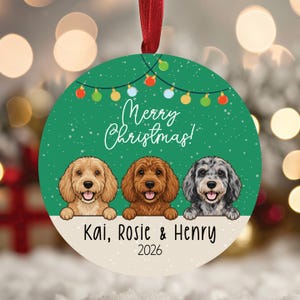 May include: A round Christmas ornament featuring a green background with white snowflakes and a string of colorful lights. Three illustrated dogs are shown with the text Merry Christmas, the names Kai, Rosie & Henry, and the year 2026.