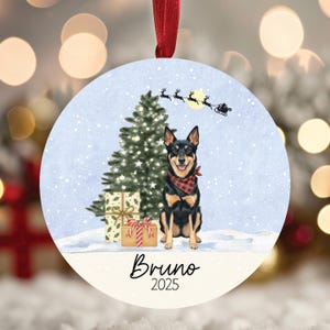 May include: Round Christmas ornament featuring a black and tan dog wearing a red plaid bandana, sitting in front of a Christmas tree and wrapped gifts. The ornament has a snowy background with Santa's sleigh and the name "Bruno 2025" at the bottom.