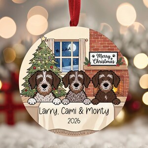 May include: A round ceramic Christmas ornament featuring an illustration of three brown and white dogs behind a table. The background shows a decorated tree, a fireplace, and a sign that reads Merry Christmas. The text Larry, Cami & Monty 2026 is printed.