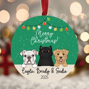 May include: Round Christmas ornament with a green background, featuring a white bulldog, a black cat, and a tan dog. The ornament says "Merry Christmas!" and has the names "Layla, Brady & Sadie" and the year "2025".