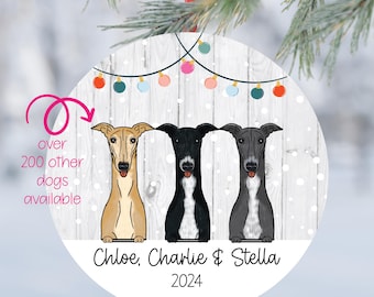 May include: Round Christmas ornament featuring three cartoon greyhounds. The ornament has a white background with a wood grain pattern and the names "Chloe, Charlie & Stella" and the year "2024". A string of colorful lights is at the top.