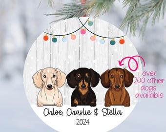 May include: A white, black, and brown dachshund Christmas ornament with a white woodgrain background. The ornament features three dachshunds with the names Chloe, Charlie, and Stella and the year 2024. The ornament also features a string of colorful lights and snowflakes. The text "over 200 other dogs available" is also included.