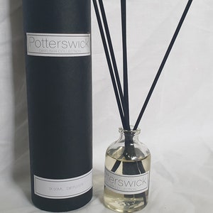 May include: A clear glass diffuser bottle with black reeds and a black cylindrical box. The bottle contains a light-coloured liquid and a label that reads "Potterswick Diffuser Collection". The box also has a label with the same text.