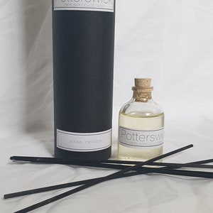 May include: A black cylindrical diffuser container and a small glass bottle with a cork top, both labelled "Potterswick Diffuser Collection." The bottle contains a light yellow liquid. Several black diffuser sticks are arranged in front.