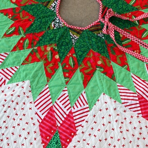 May include: A green, red, and white quilted Christmas tree skirt with a starburst design and a red and white ribbon tie.