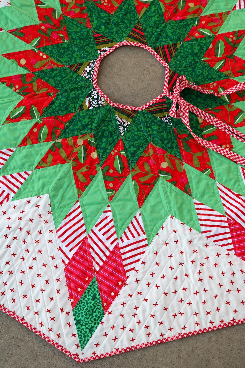 May include: A green, red, and white quilted Christmas tree skirt with a starburst design and a red and white ribbon tie.