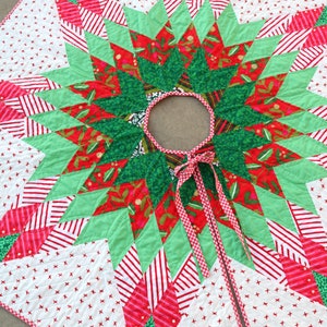 May include: A red, green, and white patchwork Christmas tree skirt with a starburst design. The skirt has a red and white gingham trim and a white ribbon tie.