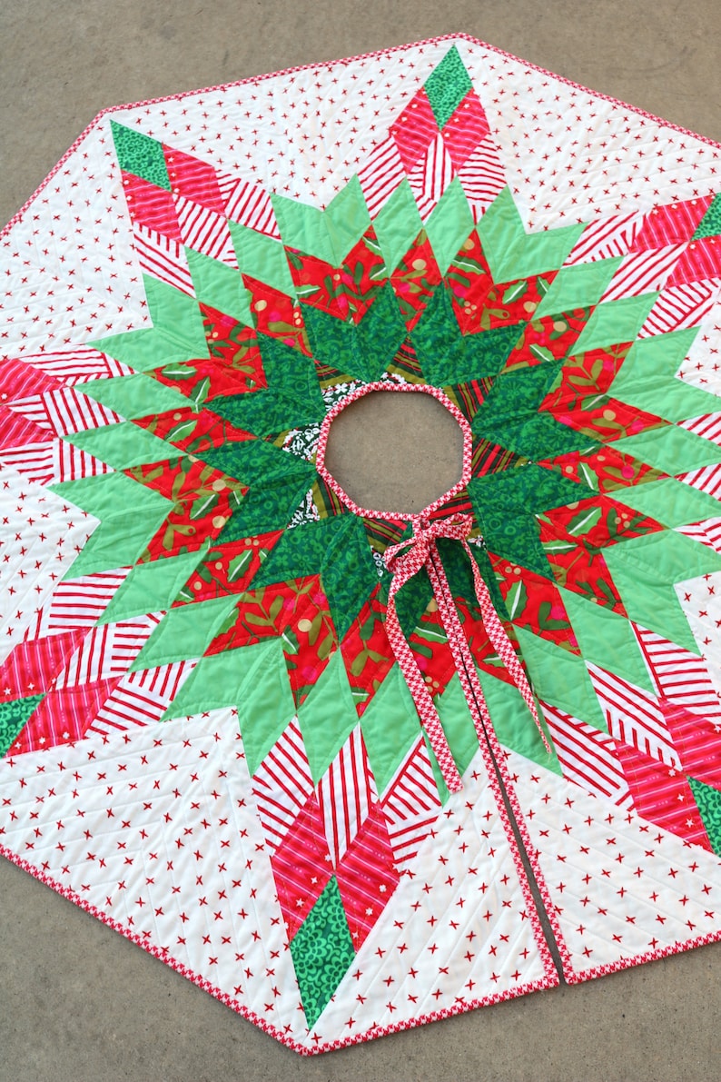 May include: A red, green, and white patchwork Christmas tree skirt with a starburst design. The skirt has a red and white gingham trim and a white ribbon tie.