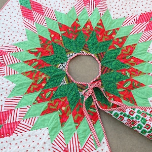 May include: A green, red, and white quilted Christmas tree skirt with a starburst design. The skirt has a red and white gingham trim and a tie closure.