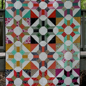 Puede incluir: Una colcha colorida con un patrón geométrico de estrellas y círculos. La colcha está hecha de varias telas en tonos de rojo, naranja, amarillo, verde, azul y morado.