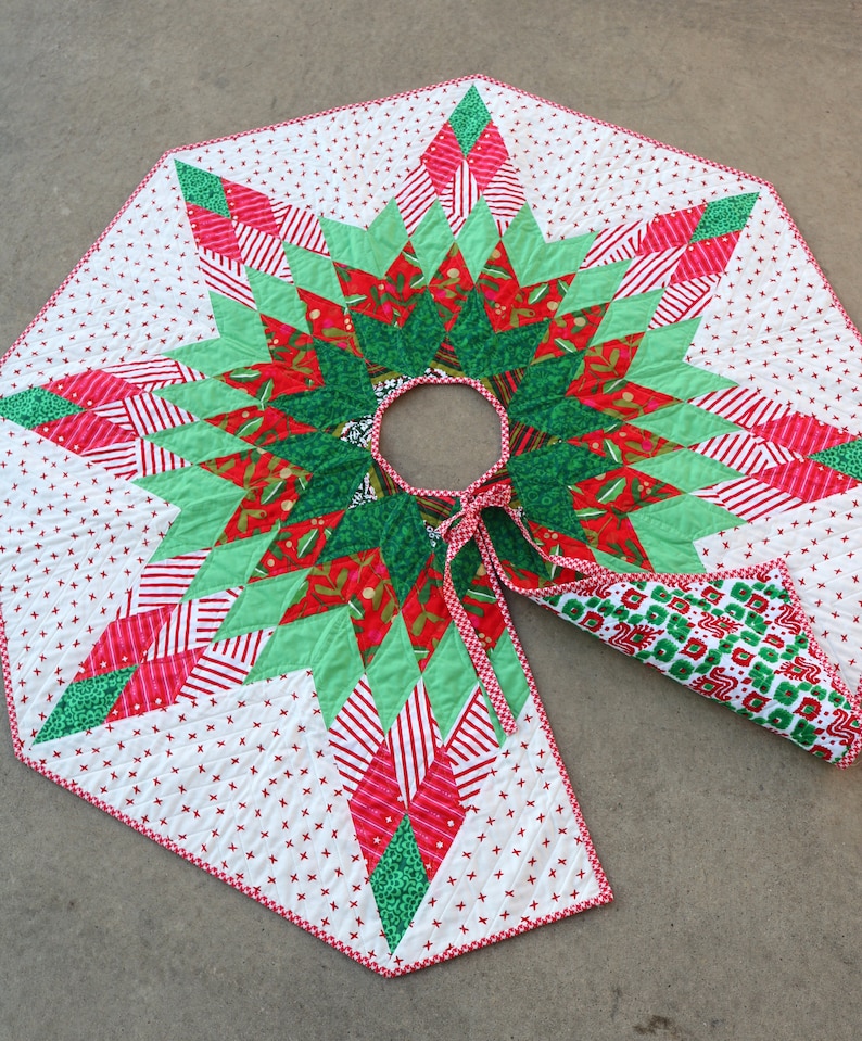 May include: A red and green quilted Christmas tree skirt with a starburst design. The skirt has a white background with red and white gingham trim.