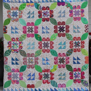 May include: A colorful quilt with a floral pattern. The quilt features large, stylized flowers in shades of pink, red, and green, with star-shaped centers. The flowers are connected by green leaf shapes, set against a cream background.