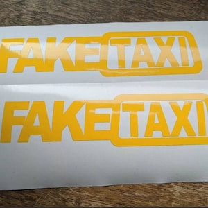 May include: Two white stickers with the text "FAKE TAXI" in yellow letters. The text is in a bold, blocky font.