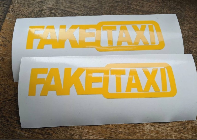 May include: Two white stickers with the text "FAKE TAXI" in yellow letters. The text is in a bold, blocky font.