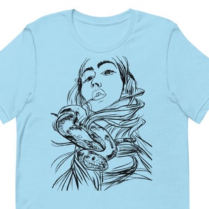 Op de afbeelding: Een lichtblauw t-shirt met een zwart-witte illustratie van een vrouw met een slang om haar nek.