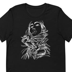 Könnte beinhalten: Schwarzes T-Shirt mit einer weißen Strichzeichnung einer Frau und einer Schlange. Die Illustration zeigt das Gesicht und die Haare der Frau, mit der Schlange, die sich um sie windet. Das Design ist mittig auf dem T-Shirt platziert.