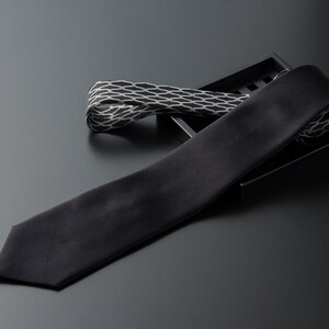 Puede incluir: Una corbata de seda negra con un patrón geométrico en una caja negra.