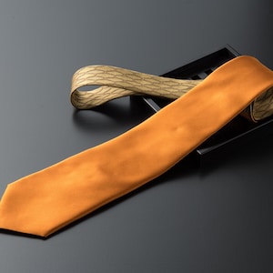 Puede incluir: Dos corbatas de seda, una naranja y otra con un patrón geométrico marrón y blanco, se muestran en una bandeja negra.