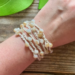 Può includere: Un braccialetto bianco all'uncinetto con perline beige e bianche. Il braccialetto è a strati e ha uno stile bohémien.