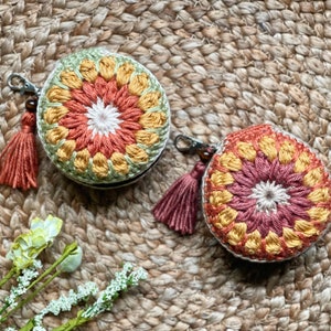 Puede incluir: Dos monederos de ganchillo con borlas. Un monedero es verde, amarillo y naranja. El otro monedero es rojo, amarillo y naranja.