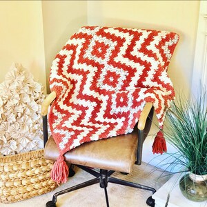 May include: A red and white crocheted throw blanket with tassels draped over a brown leather chair with a wooden frame.