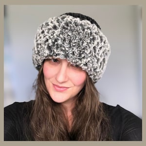 May include: A black and white faux fur hat. The hat has a black band at the top and a fluffy, textured design in shades of gray and white. The hat is designed to keep the head warm and is a stylish accessory.