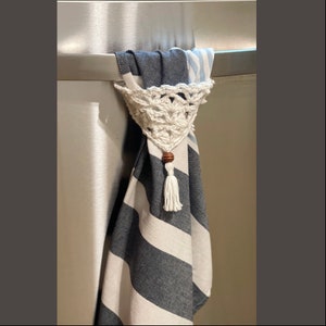 May include: A white crocheted dishcloth holder with a wooden bead and tassel hanging from a striped blue and white kitchen towel.
