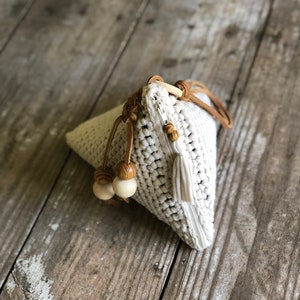 May include: A white crocheted triangular bag with a zipper closure, brown leather straps, and wooden beads. The bag has a tassel on the bottom.