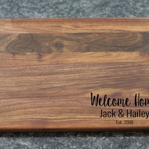 K&ouml;nnte beinhalten: Ein rechteckiges Schneidebrett aus Holz mit einer nat&uuml;rlichen Holzmaserung. Das Brett hat eine personalisierte Inschrift mit dem Text "Welcome Home Jack & Hailey Est. 2018".