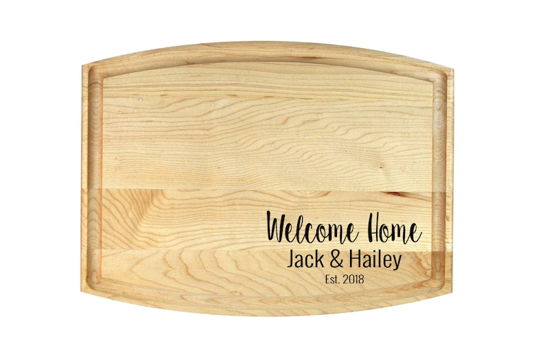 K&ouml;nnte beinhalten: Ein Schneidebrett aus Holz mit abgerundeten Kanten und einer nat&uuml;rlichen Holzoptik. Das Brett tr&auml;gt den Text "Welcome Home Jack & Hailey Est. 2018", der in die Oberfl&auml;che graviert ist.