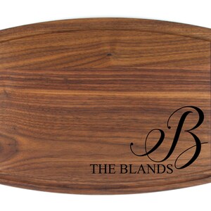 May include: A personalized walnut cutting board with a cursive "B" and the text "THE BLANDS" engraved on the surface.