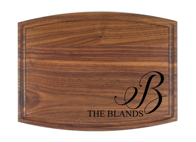 May include: A personalized walnut cutting board with a cursive "B" and the text "THE BLANDS" engraved on the surface.