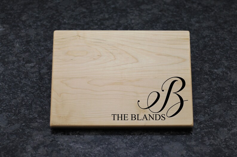 May include: A natural wood cutting board with a black engraved initial "B" and the text "THE BLANDS".