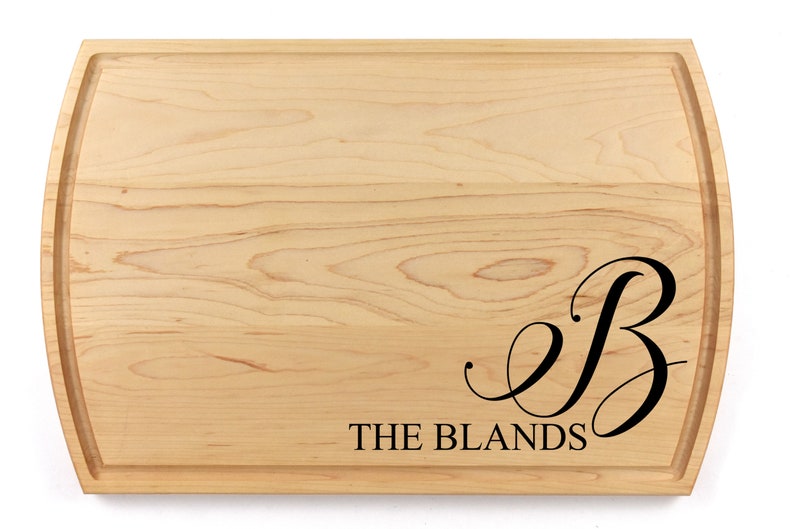 May include: A natural wood cutting board with a rounded edge. The board is engraved with the letter "B" in a cursive font and the text "THE BLANDS".