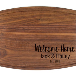 K&ouml;nnte beinhalten: Ein braunes, rechteckiges Schneidebrett aus Holz mit abgerundeten Kanten und einer Rille am Rand. Das Brett ist mit dem Text "Welcome Home Jack & Hailey Est. 2018" graviert.