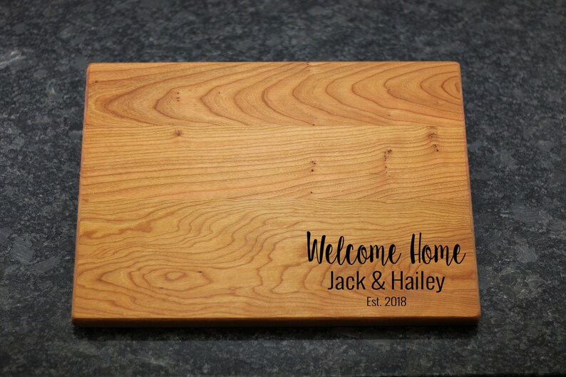 K&ouml;nnte beinhalten: Ein Schneidebrett aus Holz mit dem eingravierten Text "Welcome Home Jack & Hailey Est. 2018".