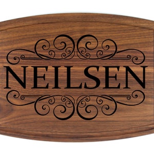 May include: A wooden cutting board with a decorative engraved design and the name "NEILSEN" in black lettering.