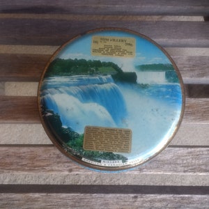 May include: A round, blue and white tin with a picture of Niagara Falls. The tin is labeled "Tom Hillery" and "American & Canadian Falls".