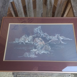 Könnte beinhalten: Gerahmter Druck einer Löwenfamilie mit einem braunen Holzrahmen. Der Druck zeigt einen Löwen mit einer vollen Mähne und mehreren Löwenjungen. Der Druck ist auf einem grauen Hintergrund.